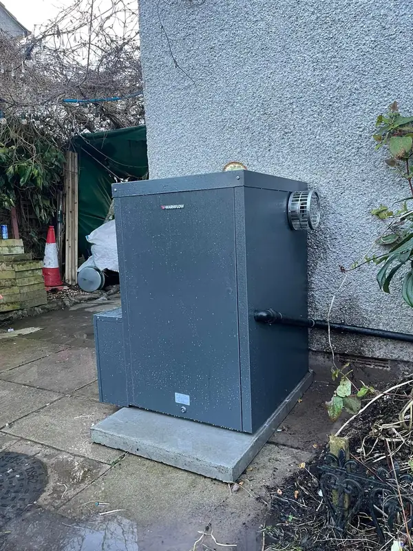 External oil boiler fitted on a concrete base beside a house, flue terminal on the side