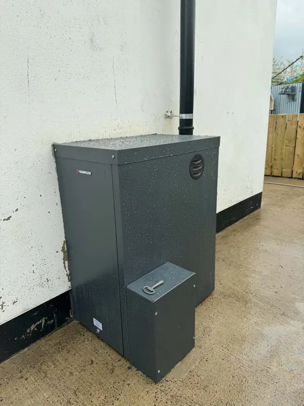 Outdoor Warmflow oil boiler on a concrete yard against a white wall
